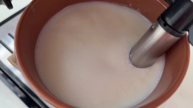 Barista steaming and frothing milk with an espresso machine steam wand for making a cappuccino or a latte, showing the vortex creation and the creamy texture of the hot milk