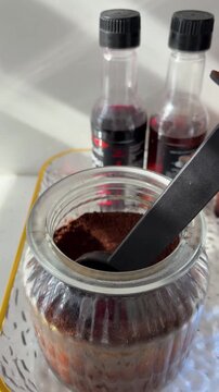 Aesthetic coffee station preparation with ground coffee in a glass jar, various flavored syrups, and a measuring spoon ready for making a delicious morning espresso drink