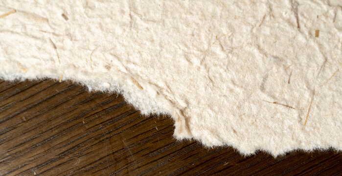 Macro close up shot of handmade recycled paper texture with rough torn edges and natural plant fibers