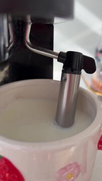 Coffee machine steam wand frothing hot milk in a ceramic mug for preparing a morning cappuccino, creating creamy foam and delicious hot beverage with a modern appliance