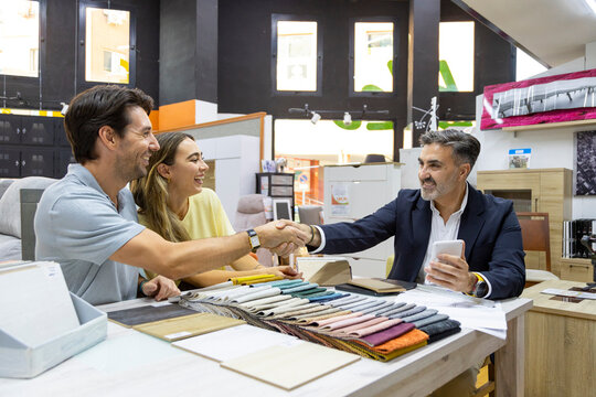 Couple shaking hands with salesman in furniture store
