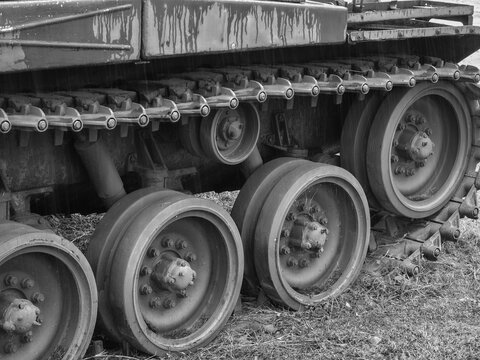 Worn steel tank wheel and track assembly in black and white, heavy machinery closeup showing rugged metal wheel bogies, bolts, mud and weathered surface textures