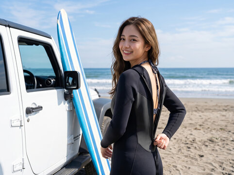 海を背景に笑顔でこちらを振り返るウェットスーツ姿の女性