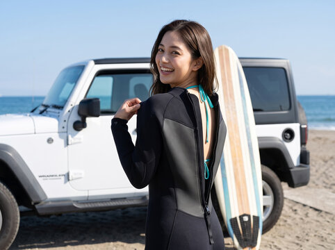 白いクロスカントリー車の横でウエットスーツを着る笑顔の女性