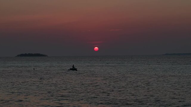 An aerial drone view of the sunset over the waters off Tanjung Gelam Beach, Karimunjawa Island. Silhouettes of tourists riding jet skis are visible.