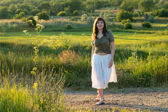 Young woman walking on a country path in a summer field during golden hour