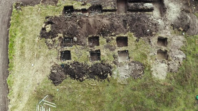 The shot gradually descends, revealing in greater detail the trenches, pits, and temporary structures excavated in the surrounding terrain