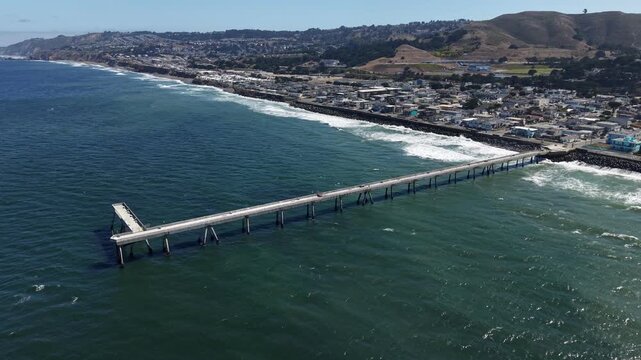 Morning drone shot over the Pacific Ocean along the Pacifica Municipal Pier, revealing the beautiful coastline and the city of Pacifica, California on a sunny day