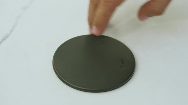 Very close-up shot showing a hand sliding the circular cover of a power outlet integrated into a white surface
