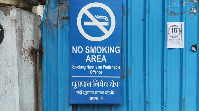 Slow tracking shot of a bilingual no smoking area signboard displaying tobacco prohibition and public health regulations at an institutional entrance