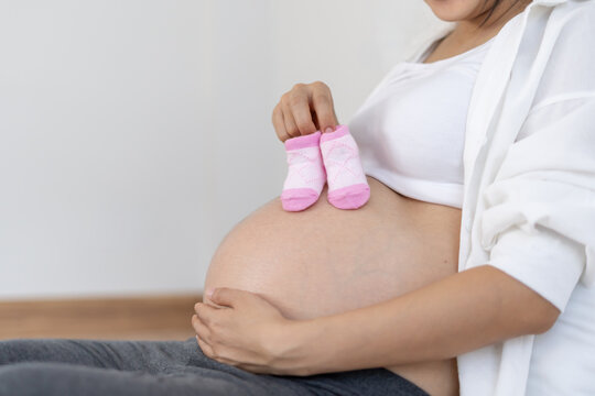 Mother is hold shoes for newborn to prepare for the upcoming baby. A pregnant woman is checking necessary for newborn and baby. Concept prepare of pregnancy readiness for mothers.