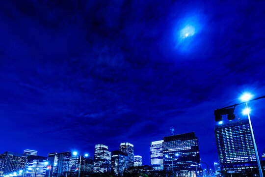 Mysterious night cityscape of Tokyo financial district under a dramatic moonlit sky.