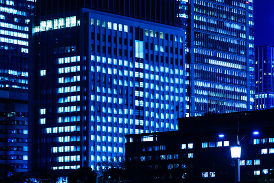 Cyber-blue illuminated office building facades in Tokyo financial district, showcasing corporate activity.