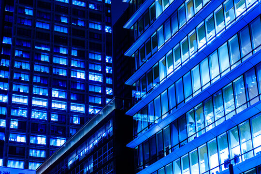 Modern glass skyscrapers at night in Tokyo financial district with glowing blue office windows and dynamic diagonal lines.