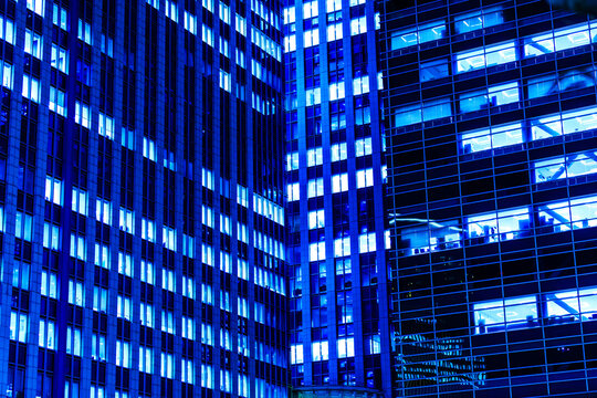 High-density abstract architectural facade of modern skyscrapers in Tokyo at night with glowing blue window grids.