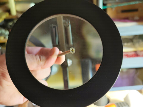 Magnifying glass inspecting a wood screw in a workshop. Close-up of hardware under magnification, concept of precision, quality control, repair, craftsmanship and DIY projects.

