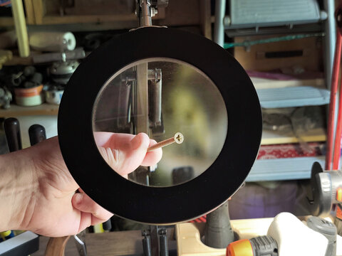 Magnifying glass inspecting a wood screw in a workshop. Close-up of hardware under magnification, concept of precision, quality control, repair, craftsmanship and DIY projects.
