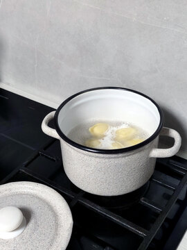 White speckled pot with boiling water and dumplings cooking on a gas stove in a home kitchen.
