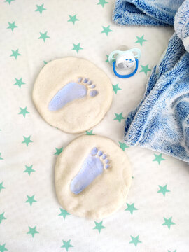 white sheet with green stars, the imprint of a child's foot on the salt dough, a blue baby pacifier, a boy child, birth, a mold of a small foot things accessories for the birth of a child, toys and 