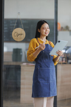 Asian cafe owner using digital tablet next to open sign