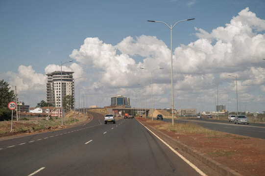 Nairobi, Kenya - 27 March 2022: View of a multi-lane highway with modern buildings, streetlights, and traffic under a cloudy blue sky.