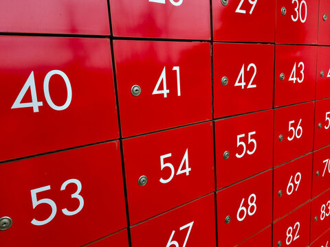 Red metal locker doors with white numbers and small round locks in repetitive grid, vibrant red color and orderly pattern creating energetic urban geometry