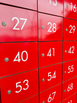 Red metal lockers with white numeric labels in grid pattern showing numbers 27 28 29 40 41 42 53 54 55 67 68, bright red glossy finish and small circular locks creating bold geometric composition