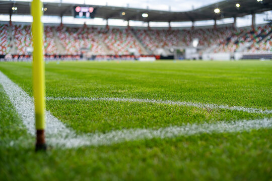 Yellow corner post flag on a professional soccer field with blurred stadium, green grass and spectators in the background during a football match.