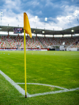 Yellow soccer corner flag on a green football field with blurred stadium and spectators under bright floodlights, creating a colorful sports background.