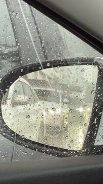 Vertical 4K video showing left passenger side wing mirror reflecting long line of cars stuck in heavy rain traffic. 