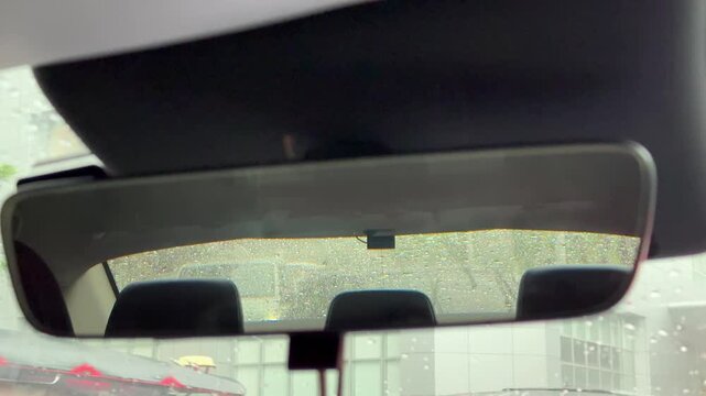 Horizontal 4K video showing rearview mirror inside car reflecting traffic lined up behind in heavy rain. 