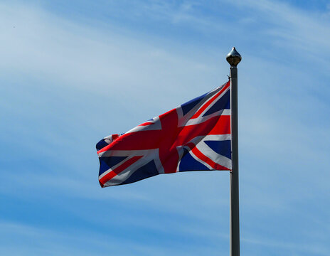 The colourful british flag hoisted on a flagpole, flutters against a blue sky