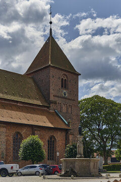 Ribe, Denmark - 20 July 2026: View of St. Catharina Church with its historic red brick architecture and tall tower, featuring a stone fountain in the foreground under a cloudy blue sky.
