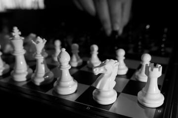 White chess knight and pieces on chessboard with hand moving piece in soft dramatic light conveying focus and strategy © CoreRock