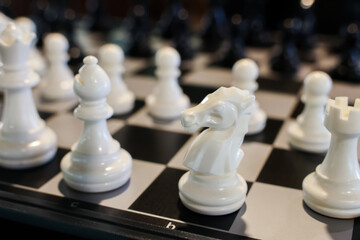 White chess knight and pieces arranged on black and white chessboard ready for play, shallow depth of field evokes quiet focus and strategy © CoreRock