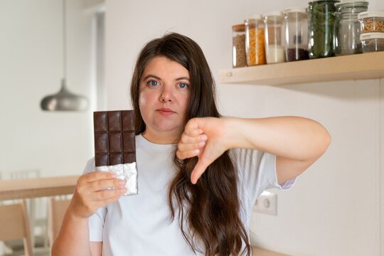 Refusal of sweet chocolate: a woman in a white t-shirt holds chocolate in foil in her hands and shows a thumbs down dislike
