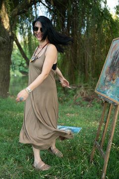 Happy woman artist painter dancing and smiling outdoor by the easel and canvas