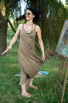 Happy woman artist painter dancing and smiling outdoor by the easel and canvas