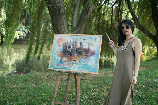 Beautiful woman painter by the river with sunglasses painting on a canvas on an easel