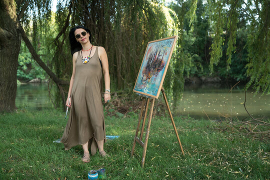Portrait of a woman artist painter outoor painting by the river in sunglasses 