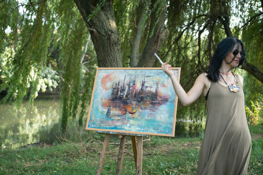 Happy woman artist painter dancing and smiling outdoor by the easel and canvas