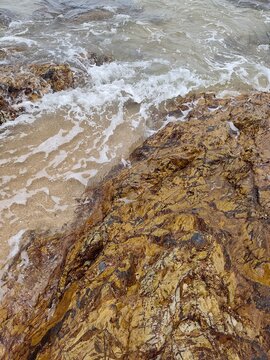 High angle view looking down at sea waves crashing against brown rocky shoreline with white foam splashing over stones.