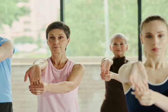 Diverse Caucasian women of different ages stretching arms during group fitness class in gym. Image represents active lifestyle and is suitable for senior wellness marketing campaigns