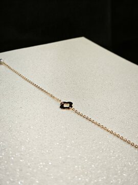 Delicate gold chain bracelet with clover charm on a sparkly white surface. Minimalist jewelry flatlay