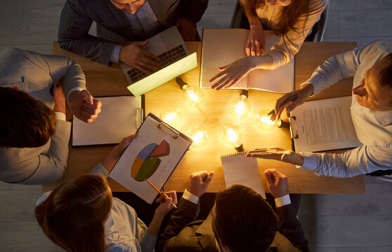 Group of coworkers in team working together in office with light bulb on table, symbolizing business inspiration and creative ideas in a professional setting with focus and collaboration.