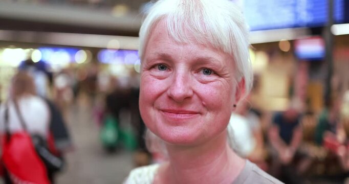 Caucasian senior woman looking at camera inside airport during evening time - Urban lifestyle and travel concept - UGC content - Main focus on face