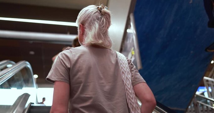 Caucasian 50's woman on escalator wearing casual clothes - City lifestyle, travel and elderly person concept - UGC content