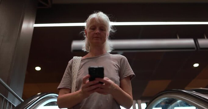 Caucasian 50's woman using smartphone on escalator at subway - City lifestyle and technology concept - UGC content