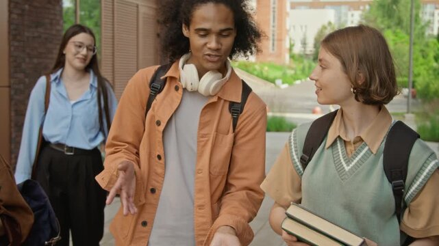 Diverse young adults walking outside college campus building, talking, laughing and giving high five. Footage is ideal for university promotional videos and student life campaigns