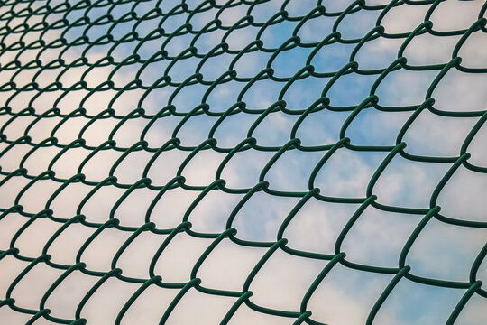 Green chain link fence pattern against a bright blue sky with white clouds
